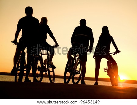 Image of sporty company  friends on bicycles outdoors against sunset. Silhouette.