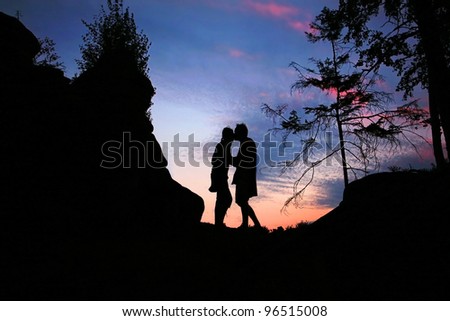 Couple kissing at sunset with colorful clouds on top of mountain peak