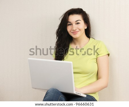 Young woman sitting with laptop near wall