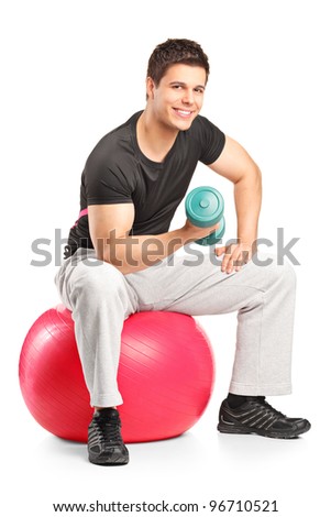 Smiling male lifting up a dumbbell seated on a fitness ball isolated on white background
