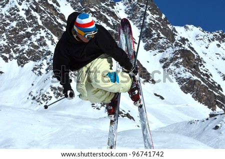free ride skier performing a jump and side grab with snow covered mountains in the background