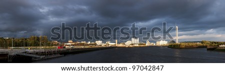 Wide and high resolution panorama of River Clyde in Glasgow showing lndmarks glowing in sunlight as stormy clouds loom.
