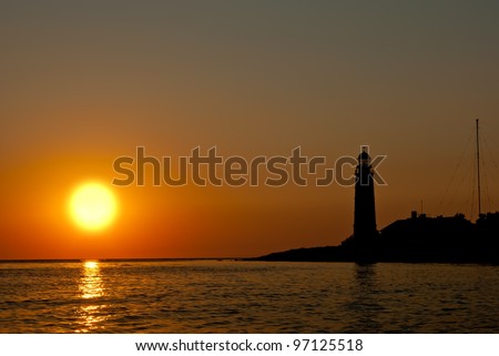Silhouette of a lighthouse on the background of a large setting sun
