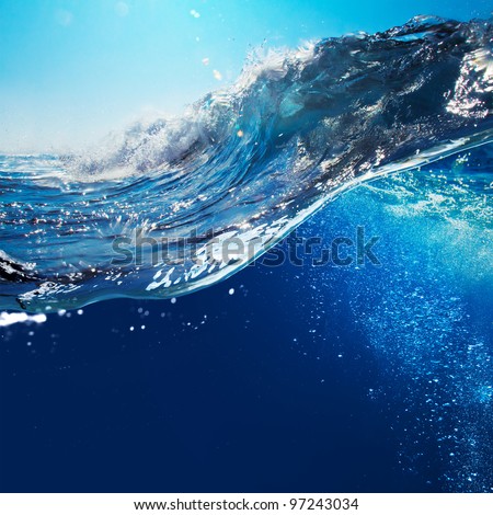ocean-view seascape landscape with blue sky and sunlight big curly ocean wave splitted by waterline to underwater part with air bubbles Royalty-Free Stock Photo #97243034
