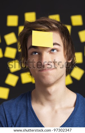 Happy student with a reminder on the head, and with more yellow paper notes in the background