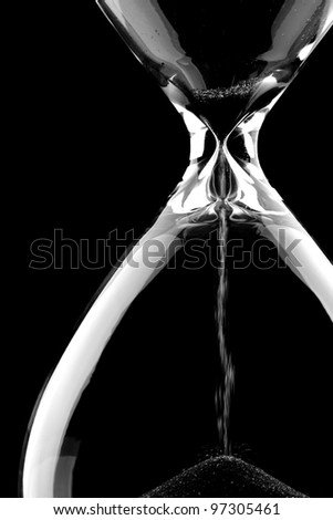 Sand flowing through an hourglass on black background concept for time running out Royalty-Free Stock Photo #97305461