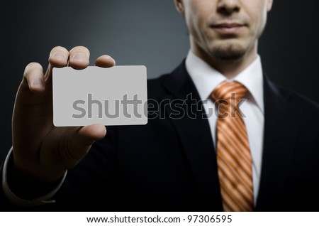 businessman in black costume and orange necktie reach out on camera and show credit card or visiting card, close up