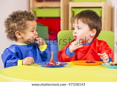Two toddlers eating fruit in a nursery