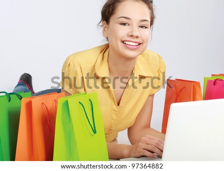 Young girl sitting with laptop near shopping bag, isolated on white background