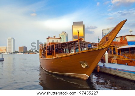 Picture of moored boats in the Arabian style against the backdrop of skyscrapers in Dubai with the reflections of the sunset.