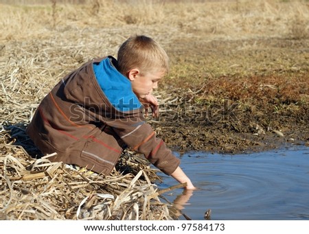 Boy playing in the mud and water of a wetland marsh, catching frogs and fish