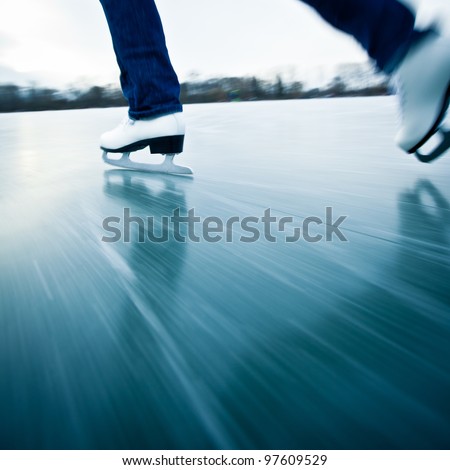 Young woman ice skating outdoors on a pond on a freezing winter day - detail of the legs (motion blur is used to convey speed; color toned image)