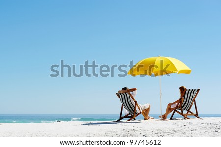 Beach summer couple on island vacation holiday relax in the sun on their deck chairs under a yellow umbrella. Idyllic travel background. Royalty-Free Stock Photo #97745612