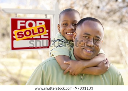 Happy African American Father and Son in Front of Sold Real Estate Sign.