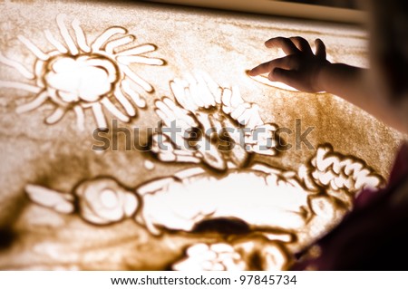 Child paint an illustration with sand on light table by finger