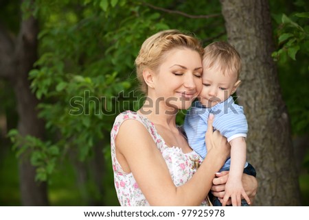 happy blond mom with her little son enjoying nature on a background of green leaves. Much of copyspace