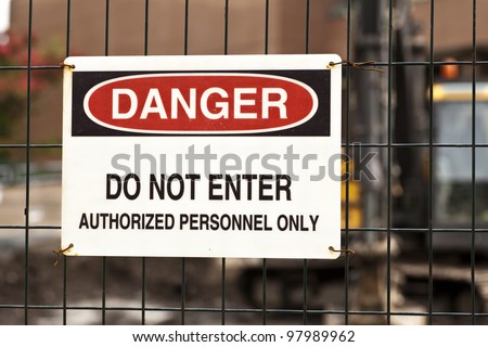 Danger sign at a work site with heavy equipment in the background.