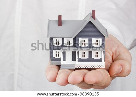 Close-up photograph of a miniature house in a man's hand.