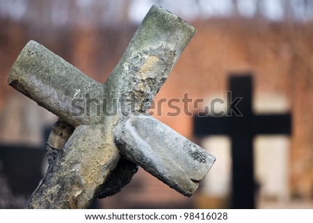 An old 19th century leaning gravestone cross at cemetery, blurred background, shallow depth of field composition