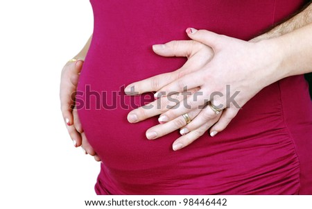 Beautiful studio shot of a 7 months pregnant married woman's belly in pink shirt with her hands and his hands intertwined, rings on both.