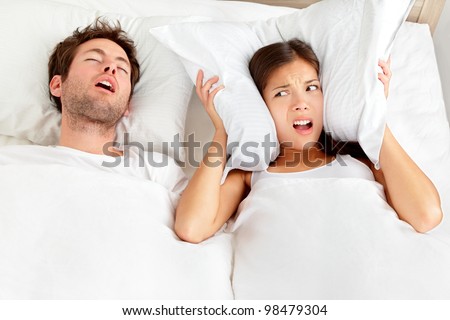 Snoring man. Couple in bed, man snoring and woman can not sleep, covering ears with pillow for snore noise. Young interracial couple, Asian woman, Caucasian man sleeping in bed at home. Royalty-Free Stock Photo #98479304