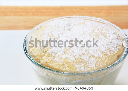Yeast dough in a glass bowl sprinkled with flour