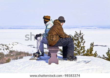Two snowboarders resting on top of mountain against the backdrop of a beautiful winter landscape. Back to back.