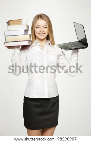 Young female holding heavy stack of books in one hand and laptop in another, isolated on gray background