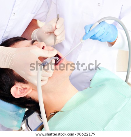 A dentist and a nurse curing young man`s teeth