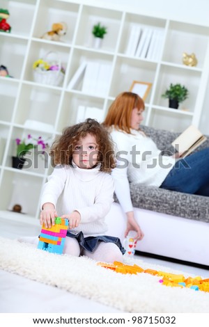 Cute girl playing with  cubes blocks , mother on sofa reading book