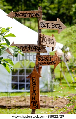 A very cool and unique wedding sign showing guests directions to various areas and a tent in the background.