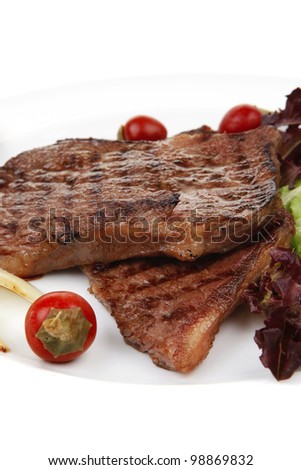 meat food : two roast steak boneless with red and chili peppers, served on green lettuce salad on dish isolated over white background