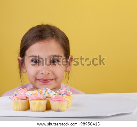 Young girl staring cross eyed at a bunch of cupcakes  on a yellow background