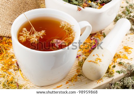 cup of healthy tea, mortar and pestle with healing herbs on wooden table, herbal medicine