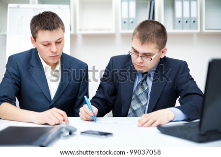 Two young business people sitting at desk working in team together, working with documents sign up contract
