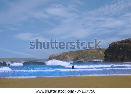beautiful clean atlantic ocean with lone surfer catching the waves with cliffs in background on Ireland's coast
