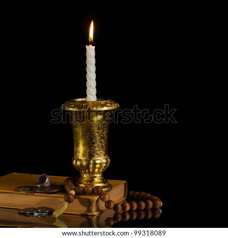 Candle with rosary, antique book and coins