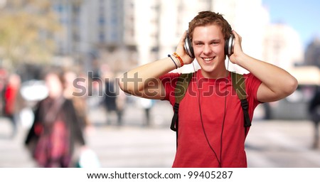 portrait of cheerful young student listening music with headphones at crowded street