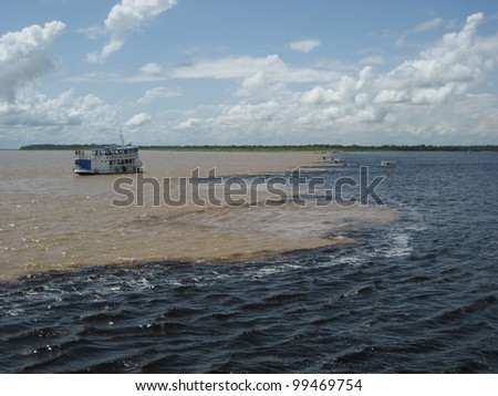 The Meeting of Waters (Portuguese: Encontro das Aguas) is the confluence between the Rio Negro, a river with dark (almost black coloured) water, and the sandy-coloured Amazon River or Rio Solimoes. Royalty-Free Stock Photo #99469754