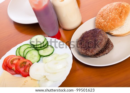 Detail of kitchen table with hamburgers and vegetable.