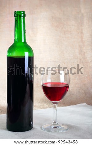 bottle with red wine and a glass against a sacking