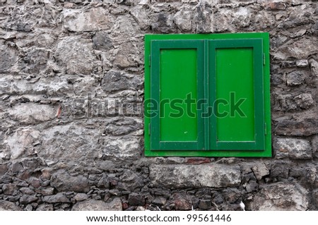 stony house wall with a green closed window