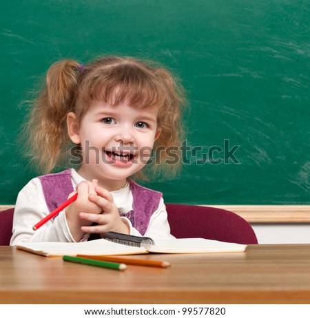 Cheerful smiling child with a book  against blackboard  in a class . Looking at camera. School concept