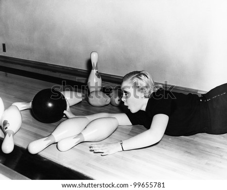 Woman sliding down bowling alley with ball