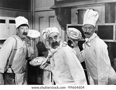 Three chefs holding pies for a fight in the kitchen Royalty-Free Stock Photo #99664604