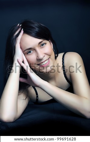 portrait of a young smiling brunette  woman with arms crossed under her hair on dark black background