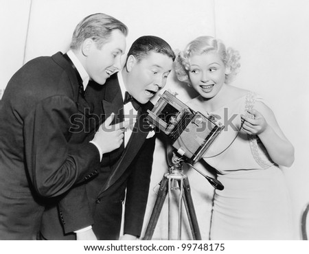 Three people looking through a camera and laughing
