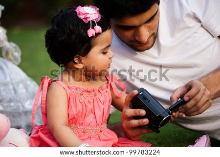father showing pictures to his daughter on digital camera, biracial family
