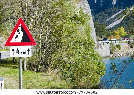 dangerous curve between mountain and austrian alps lake with alert sign