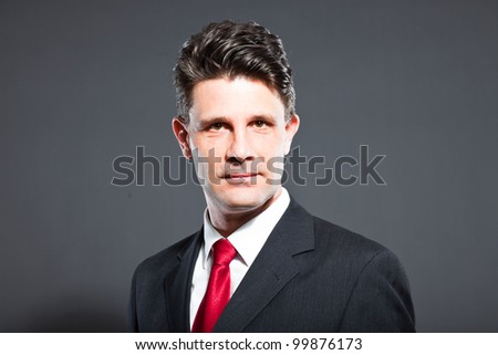 Business man with grey suit and red tie isolated on dark background. Studio shot.